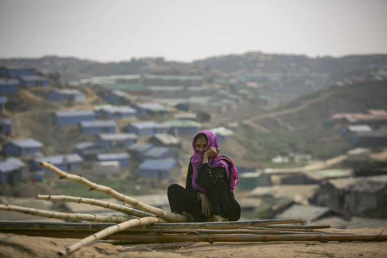 Women sits in the foreground covering her face with headscarf